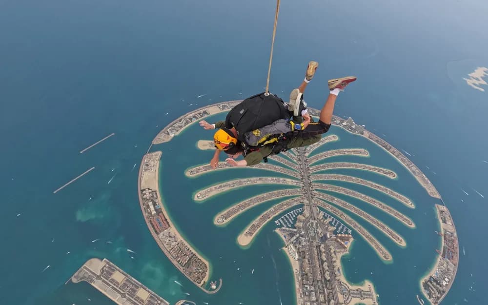 Palm Jumeirah adası üzerinde paraşütle atlayan kişi, altında turkuaz deniz