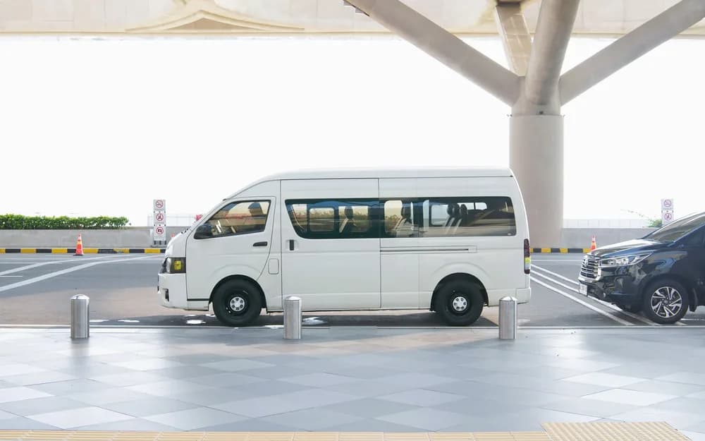 Modern havalimanı terminali önünde bekleyen temiz beyaz transfer minibüsü