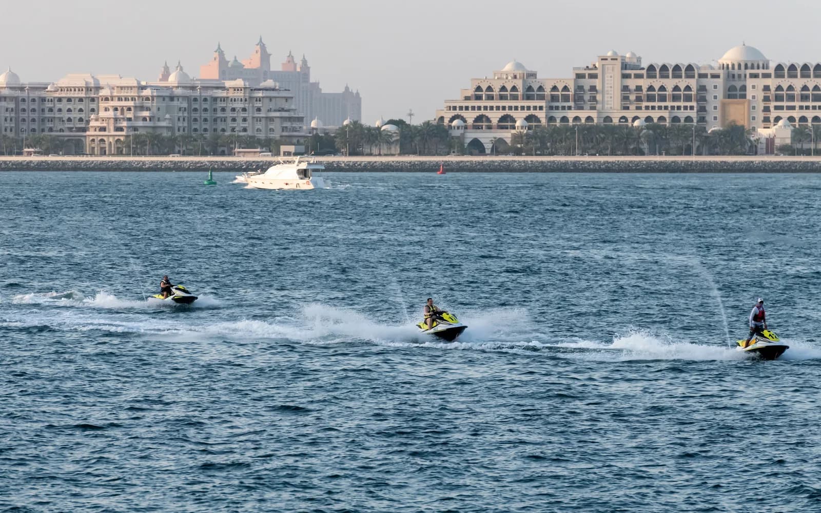 Dubai kıyısında hareket hâlindeki üç jetski ve arkada Palm Jumeirah otelleri