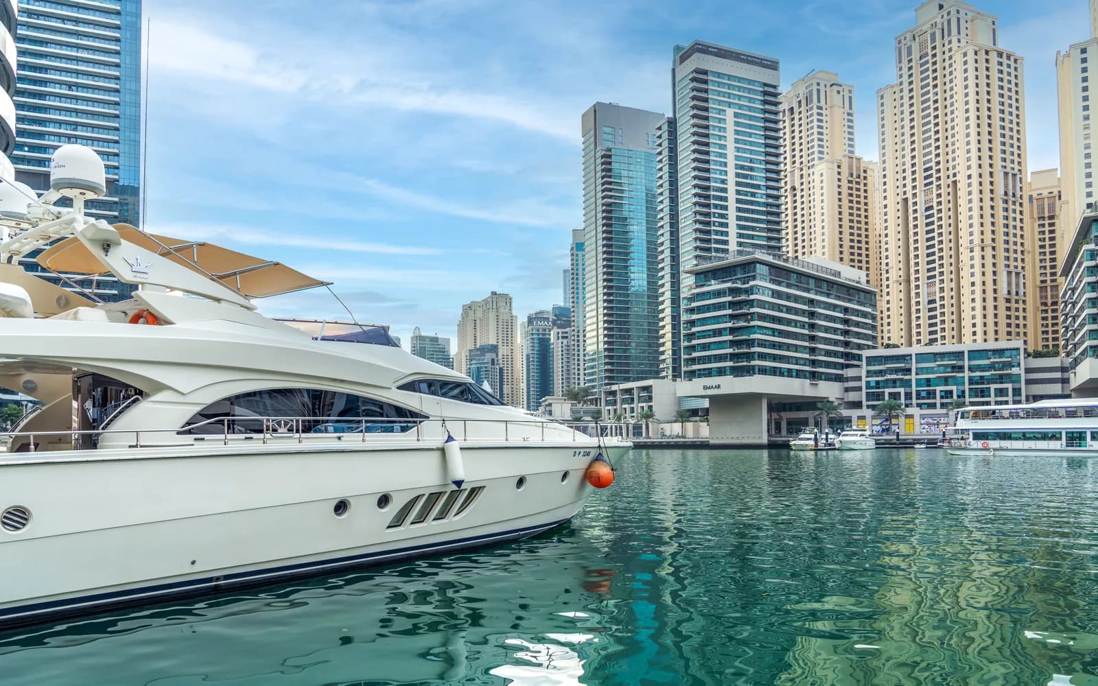 Dubai Marina'da yanaşmış beyaz lüks yat ve arkada marina gökdelenleri, turkuaz su
