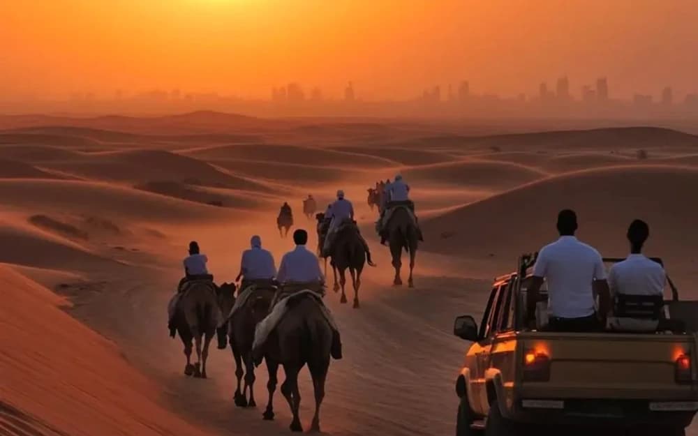 Gün batımında çölde deve kervanı ve safari aracı, ufukta Dubai silüeti
